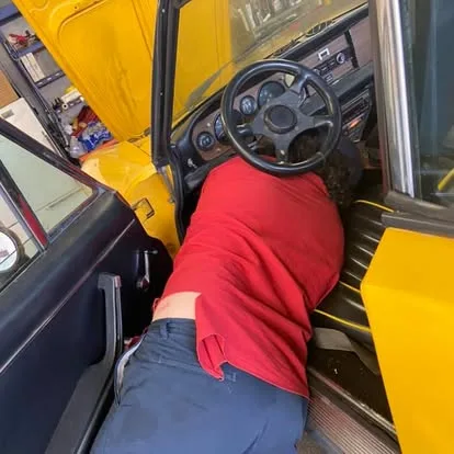 Technician working under the dash of a yellow classic car
